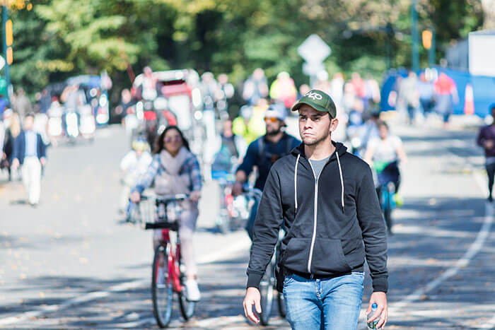 One young serious, thinking man in Midtown Manhattan with people walking on Central Park road in traffic, running, bicycles, bikes on sunny day NYC