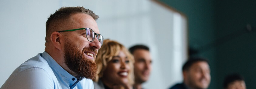 Smiling businessman and unrecognizable multi-ethnic employees sitting in a row at their company desk and listening to their boss.