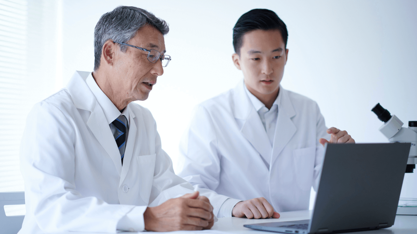Two doctors in lab coats looking at a laptop, using AI to help with diabetic eye screening